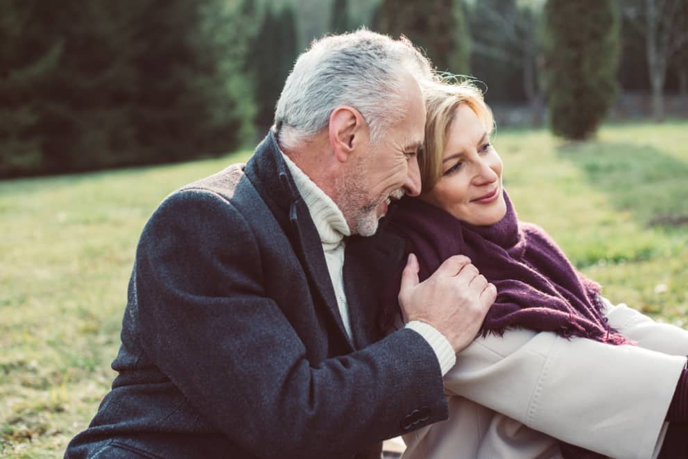 Mature man and woman are sitting on the grass close to each other and smiling.